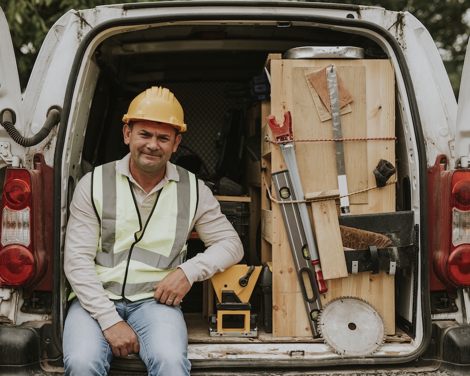 A man in high-visibility vest and a hard hat is sitting in a van full of tools