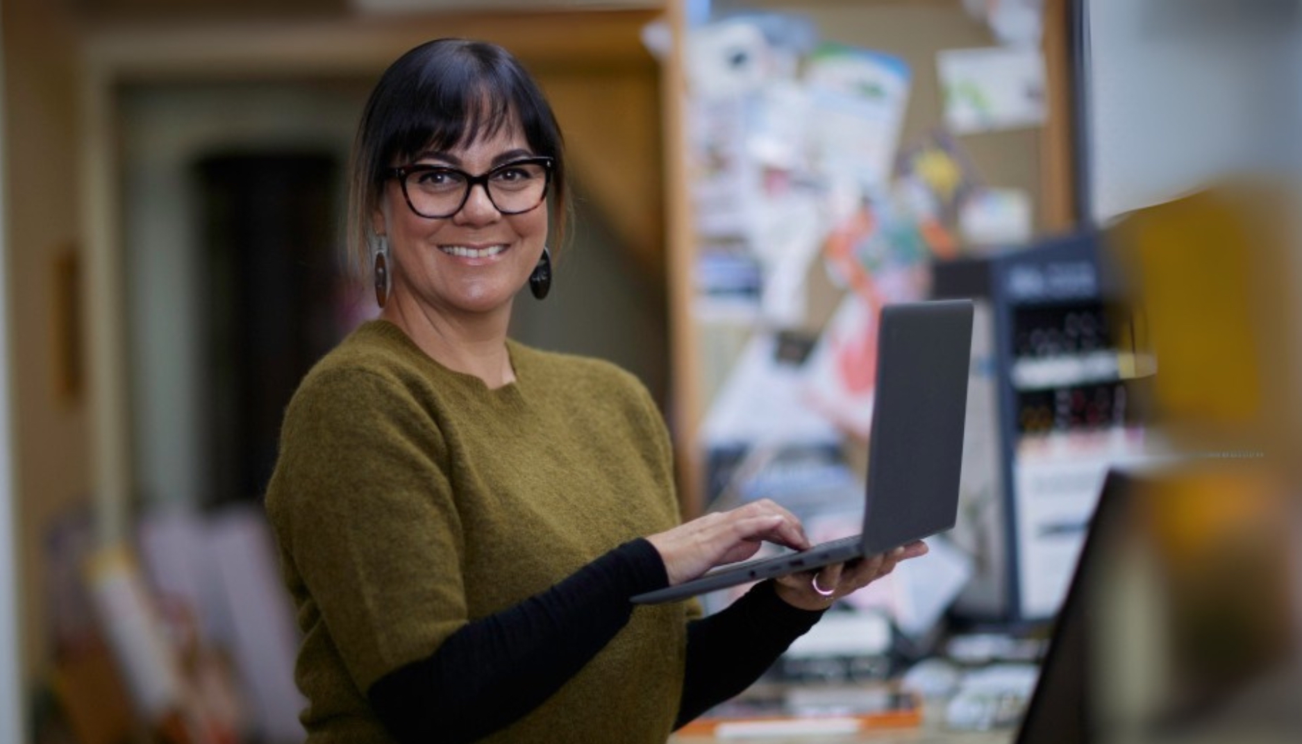 A smiling middle-aged woman looking at the camera, holding her laptop